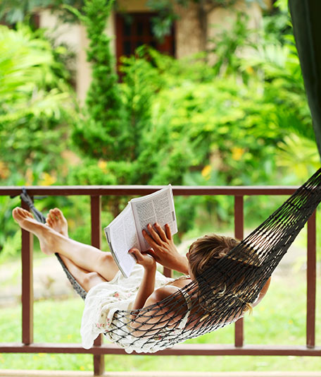 A person spends time reading a book in a hammock.